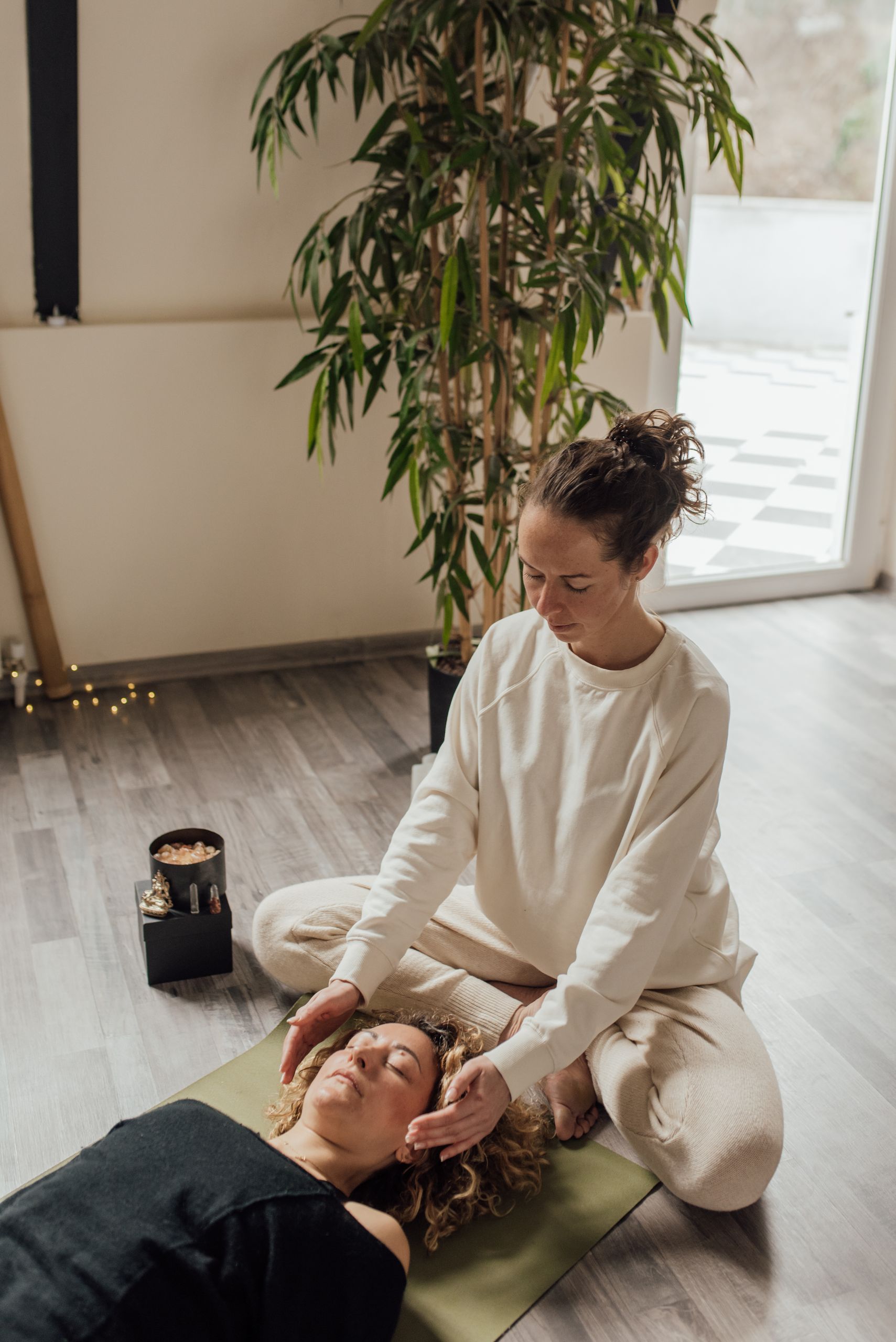 A calming scene depicting a woman practicing Reiki therapy on another woman lying on a yoga mat indoors.
